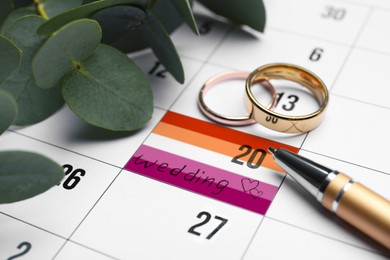 Calendar with date reminder in color of lesbian flag about Wedding Day, pen and rings, closeup