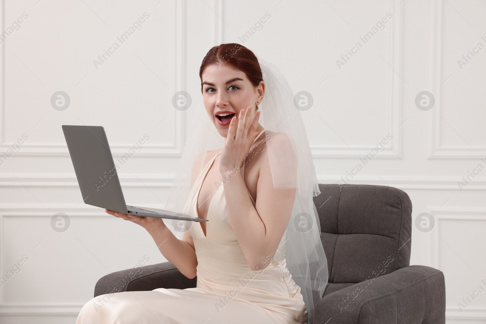 Photo of Surprised bride with laptop sitting in armchair indoors