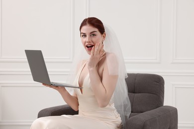 Photo of Surprised bride with laptop sitting in armchair indoors
