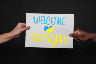 Woman and African American man holding sign with phrase WELCOME REFUGEES on black background, closeup