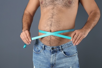 Photo of Overweight man with measuring tape on gray background, closeup