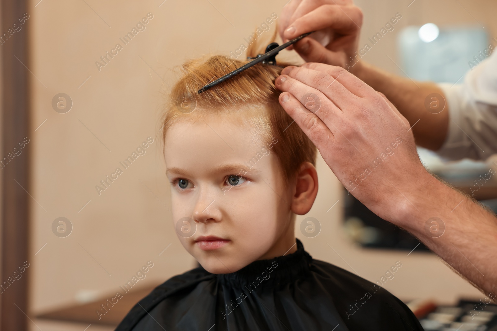 Photo of Professional hairdresser combing boy's hair in beauty salon, closeup