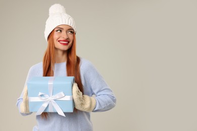 Photo of Young woman in hat and sweater with Christmas gift on light grey background, space for text