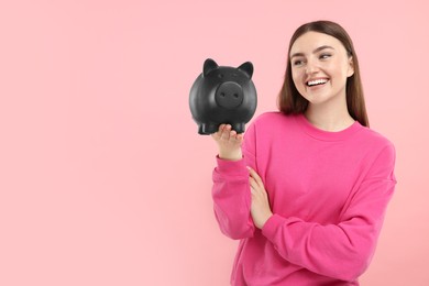 Happy woman with piggy bank on pink background, space for text