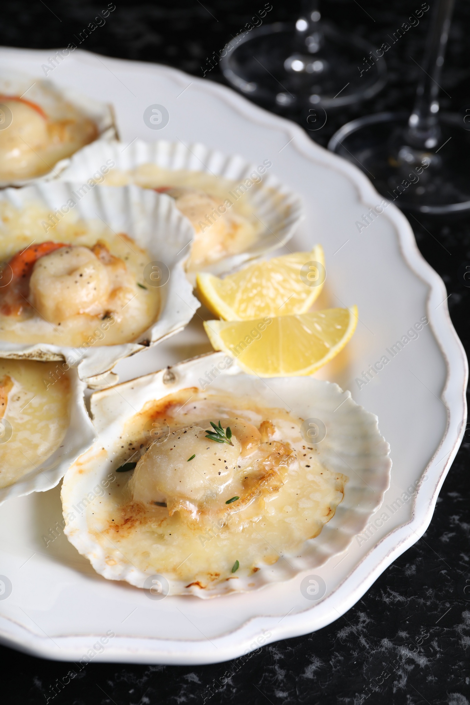 Photo of Fried scallops in shells and lemon on black textured table, closeup