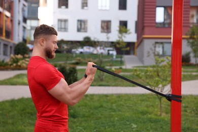 Photo of Muscular man doing exercise with elastic resistance band outdoors
