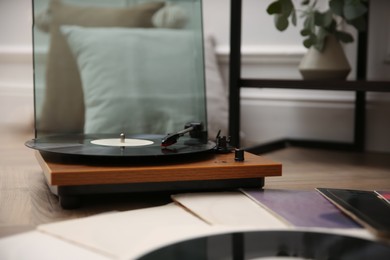 Photo of Stylish turntable with vinyl records on floor indoors