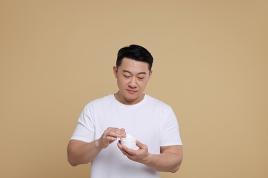 Photo of Handsome man with jar of body cream on light brown background