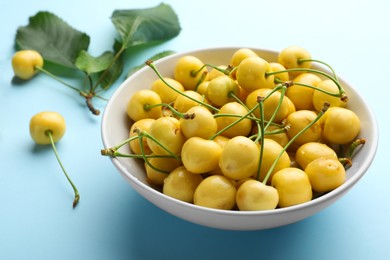 Bowl and ripe yellow cherries with green leaves on turquoise background, closeup