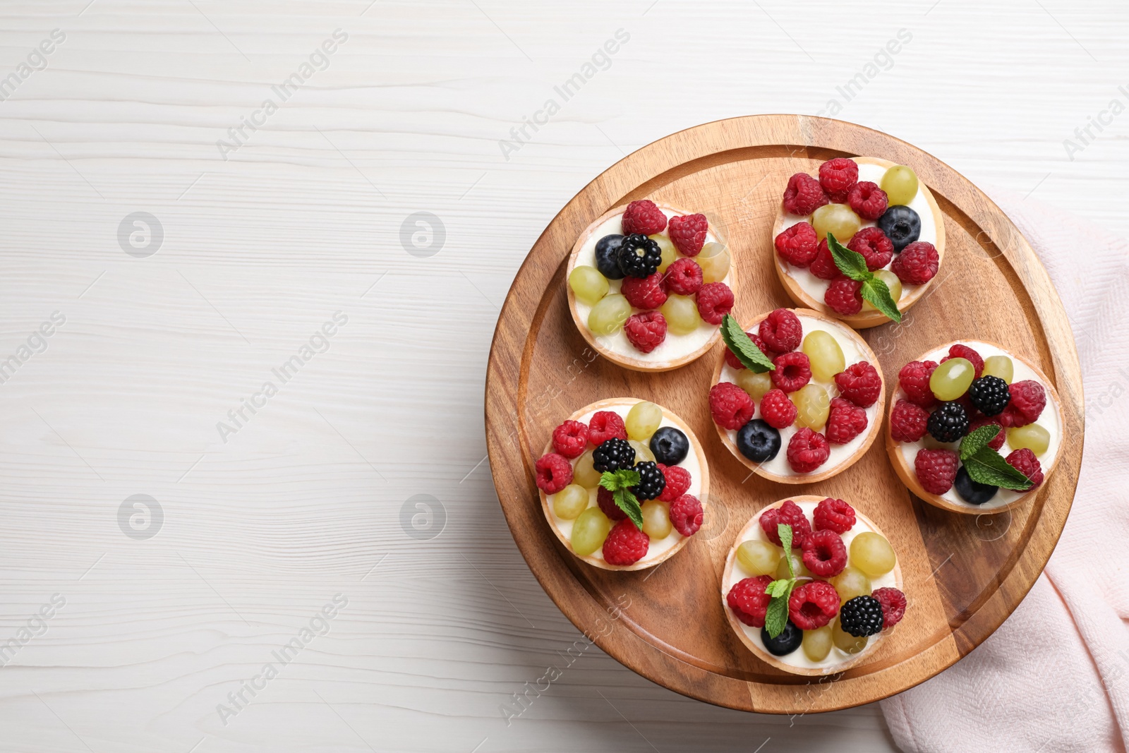 Photo of Delicious tartlets with berries on light wooden table, top view. Space for text