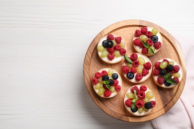 Photo of Delicious tartlets with berries on light wooden table, top view. Space for text