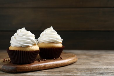 Delicious cupcakes with cream on wooden table. Space for text