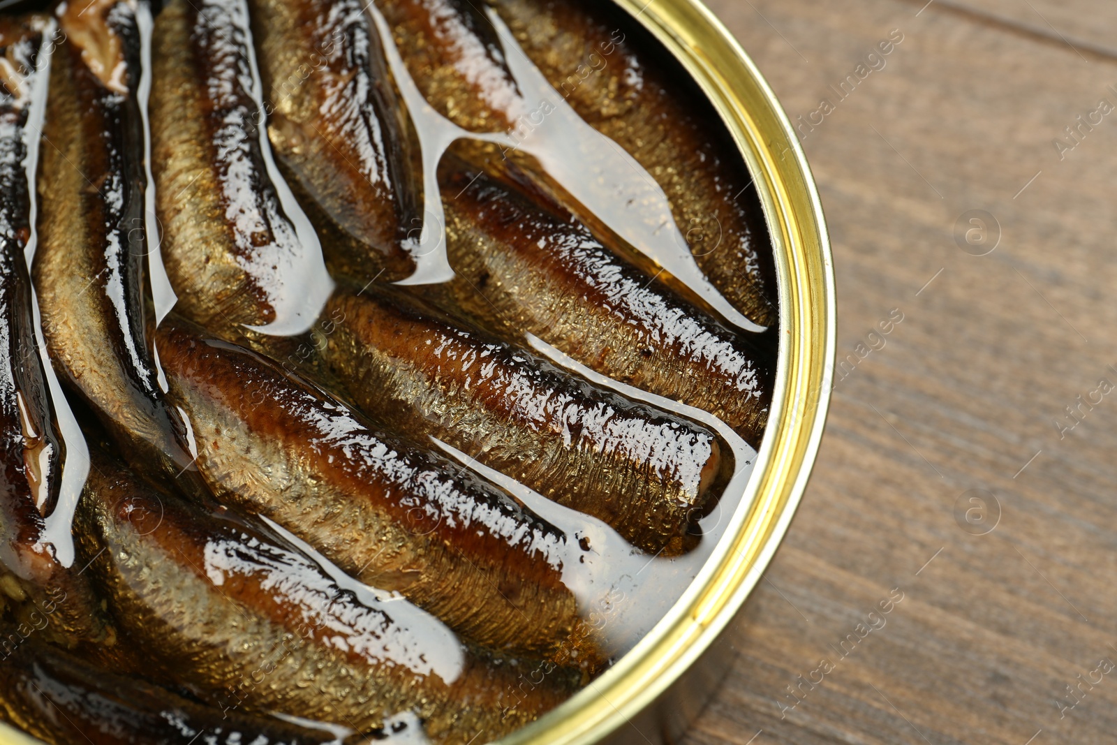 Photo of Sprats in tin can on wooden table, closeup. Space for text