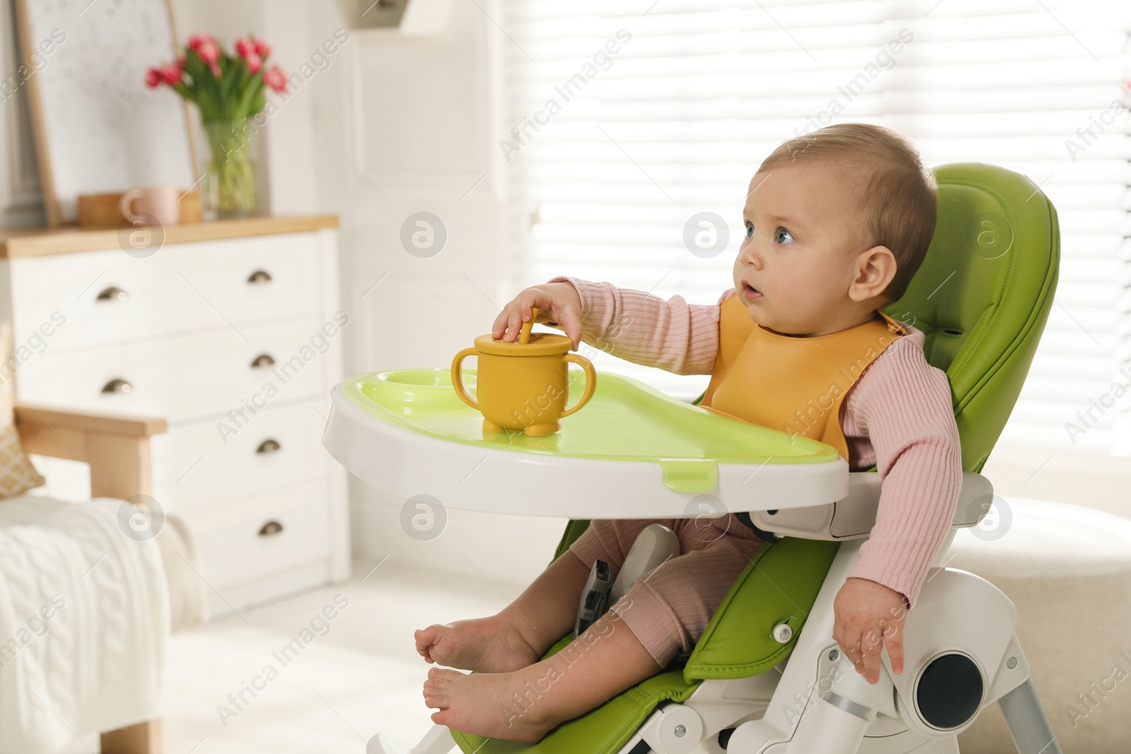 Photo of Cute little baby wearing bib in highchair at home