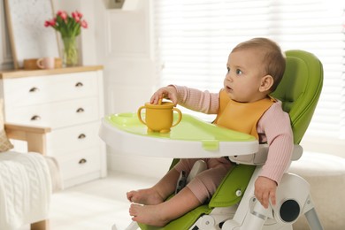 Photo of Cute little baby wearing bib in highchair at home