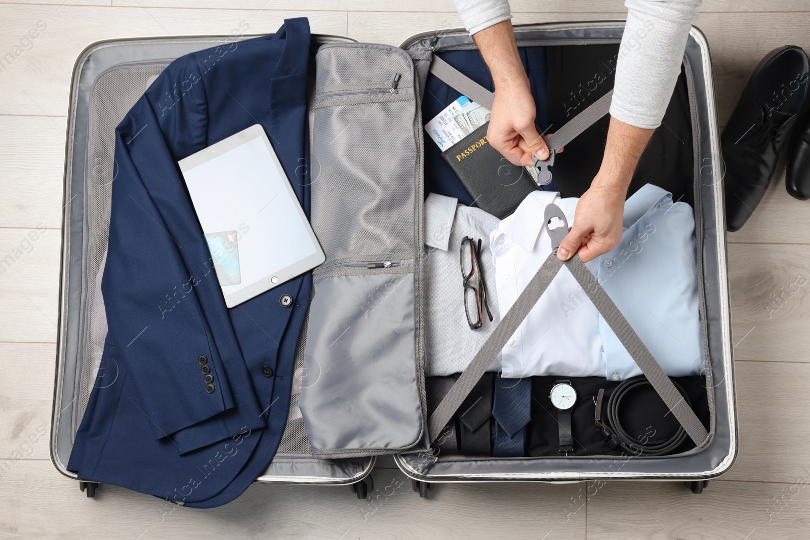 Photo of Man packing suitcase for business trip on wooden floor, top view