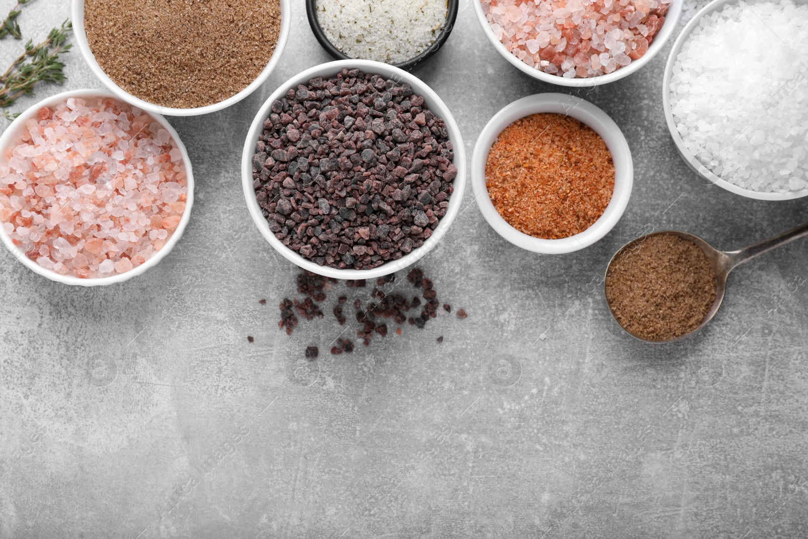 Photo of Different kinds of salt on grey table, flat lay. Space for text