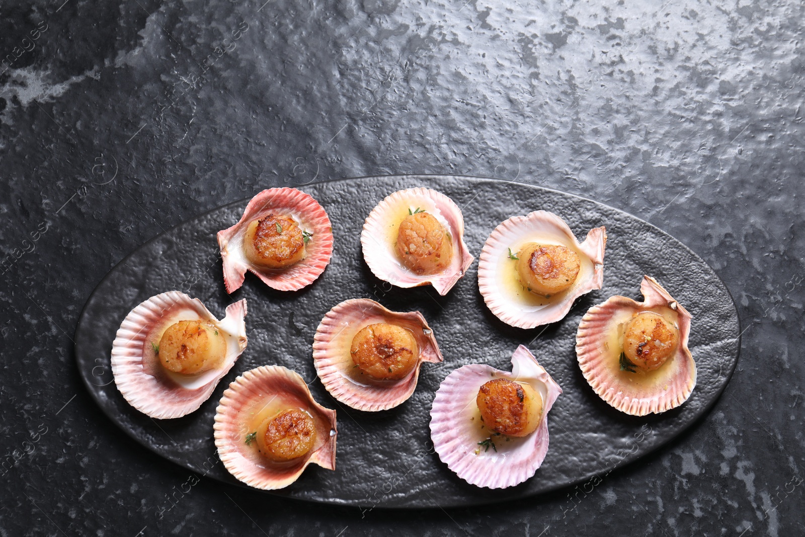 Photo of Delicious fried scallops in shells on black table, top view