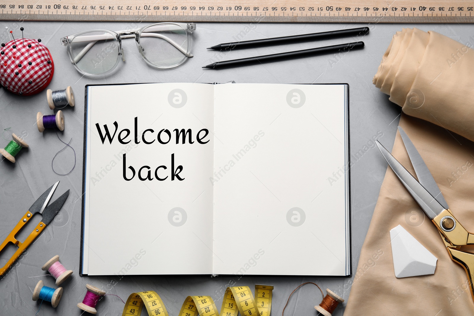 Image of Notebook with phrase Welcome Back and sewing accessories on grey background, flat lay