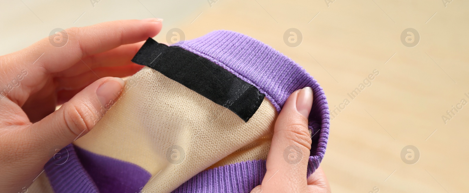 Image of Woman holding sweater with blank clothing label on blurred background, closeup. Banner design