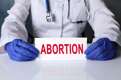 Image of Doctor holding paper card with word Abortion at white table, closeup