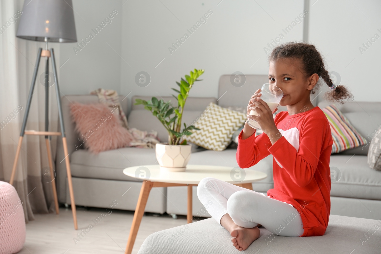 Photo of Adorable African-American girl with glass of milk at home