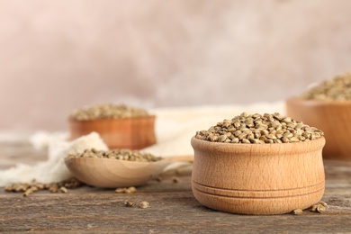 Photo of Bowl of hemp seeds on wooden table against color background