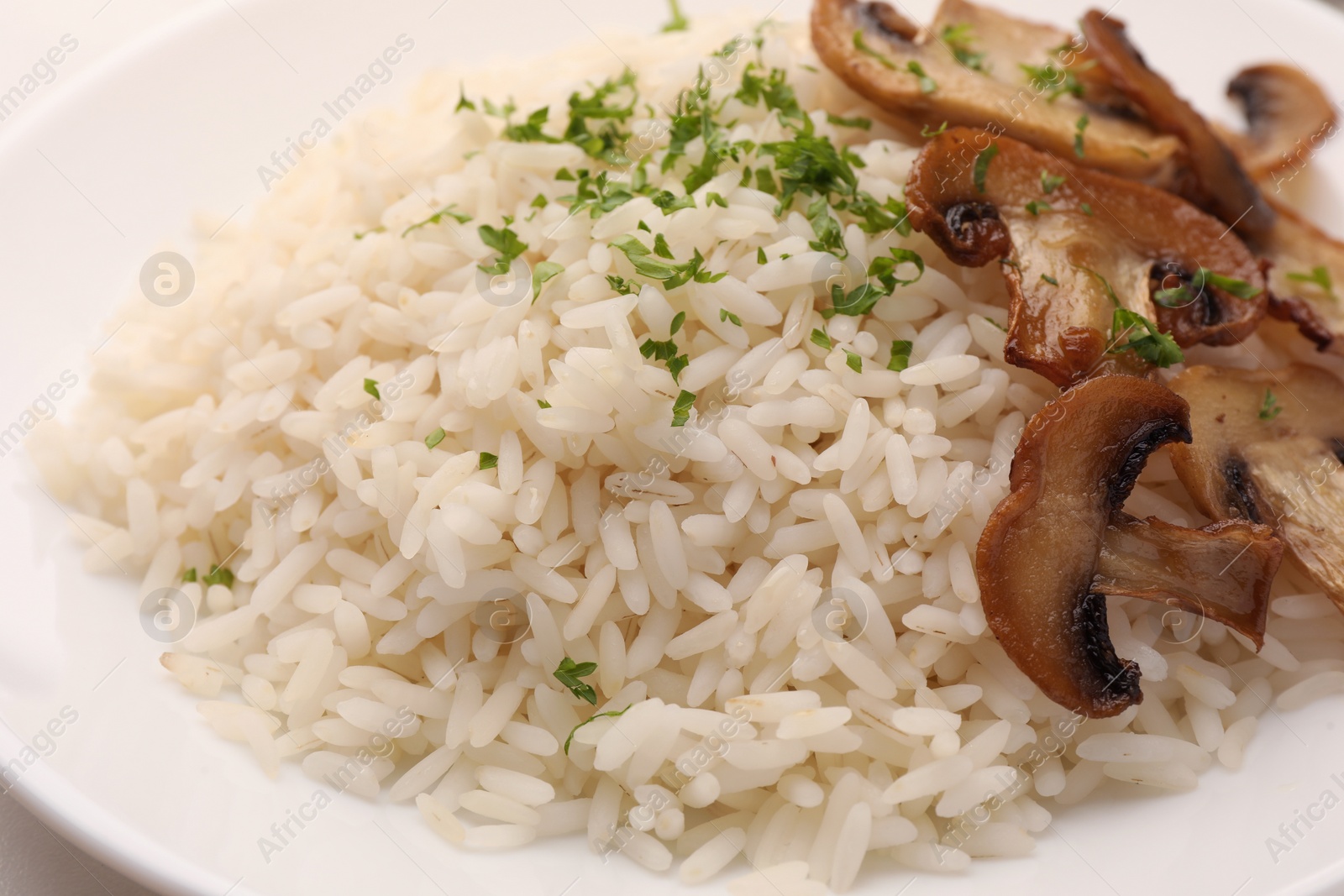 Photo of Delicious rice with parsley and mushrooms on white plate, closeup