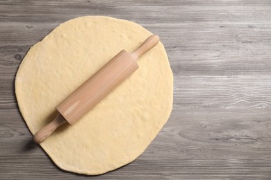 Photo of Raw dough and rolling pin on wooden table, top view. Space for text