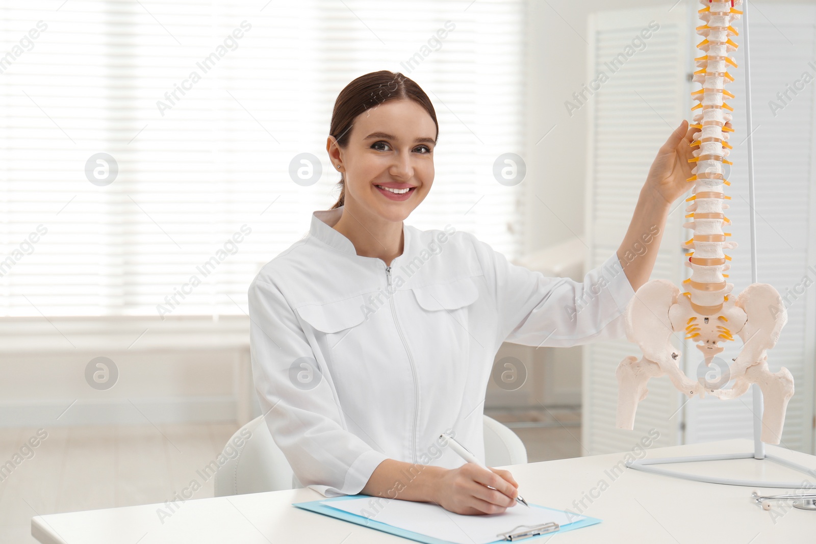 Photo of Female orthopedist at table near human spine model in office