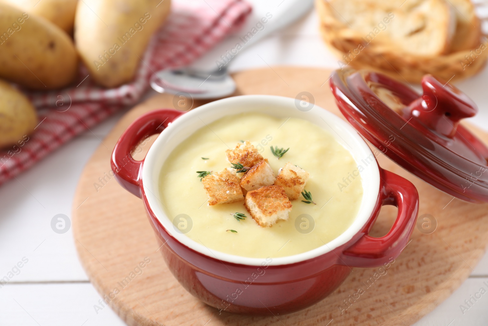 Photo of Tasty potato soup with croutons and rosemary in ceramic pot on white table, closeup