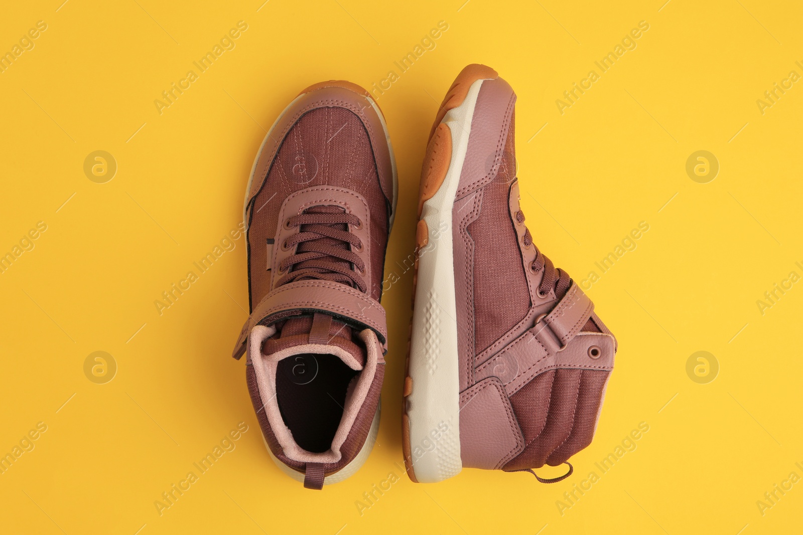 Photo of Pair of stylish kid's sneakers on yellow background, top view