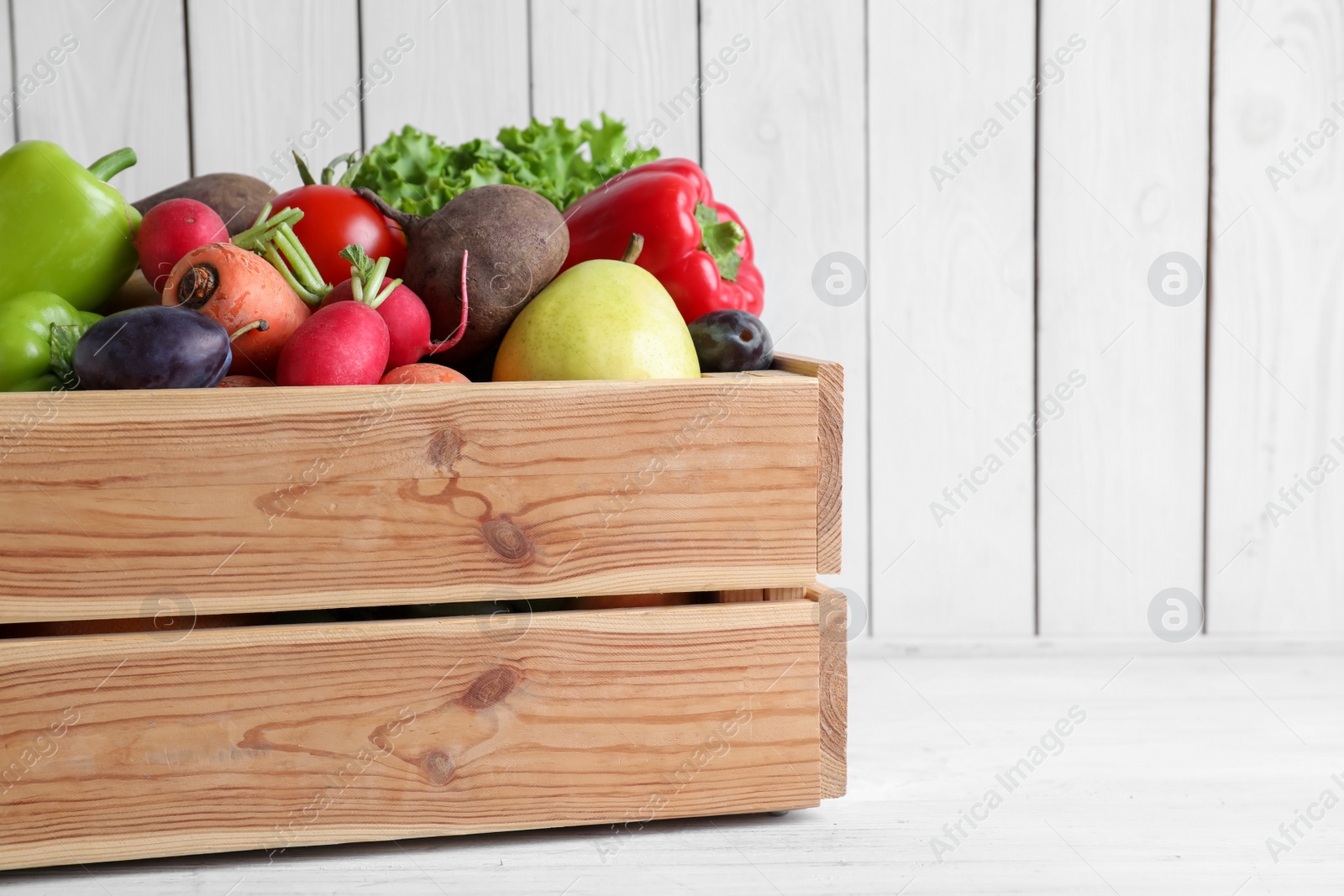 Photo of Crate full of different vegetables and fruits on white wooden table, space for text. Harvesting time