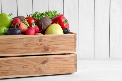Crate full of different vegetables and fruits on white wooden table, space for text. Harvesting time