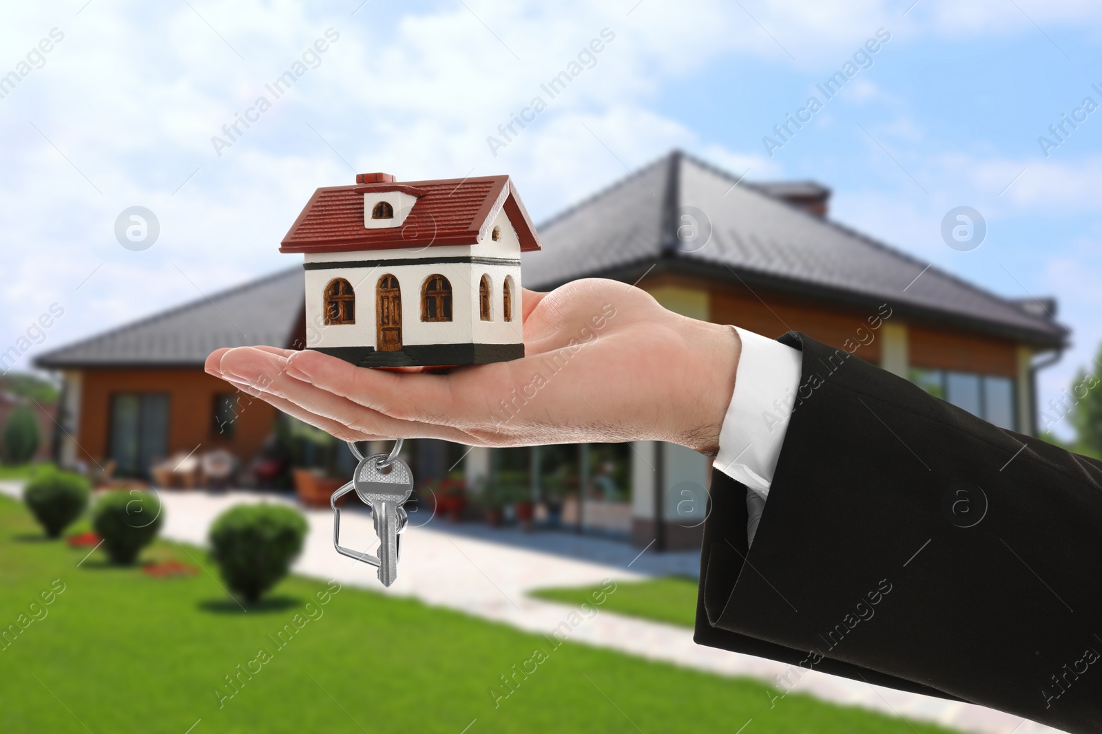 Image of Real estate agent holding key and house model against beautiful villa, closeup