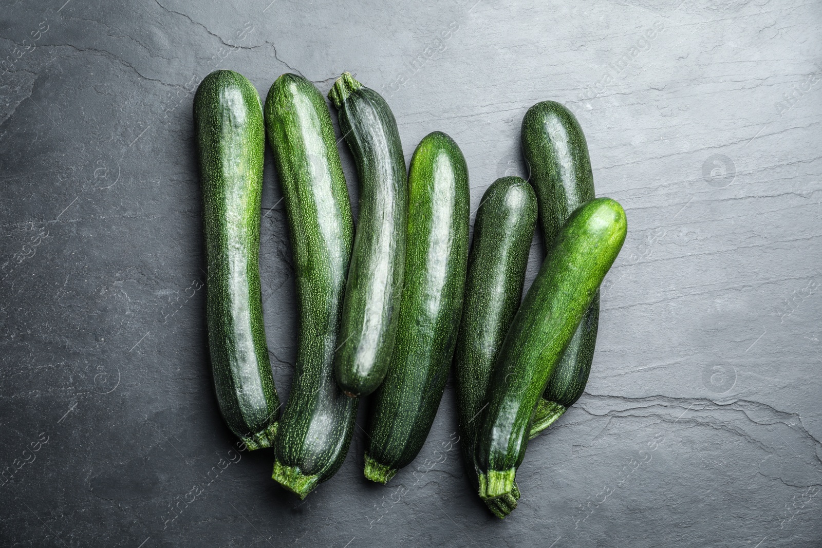 Photo of Green ripe zucchinis on black slate table, flat lay
