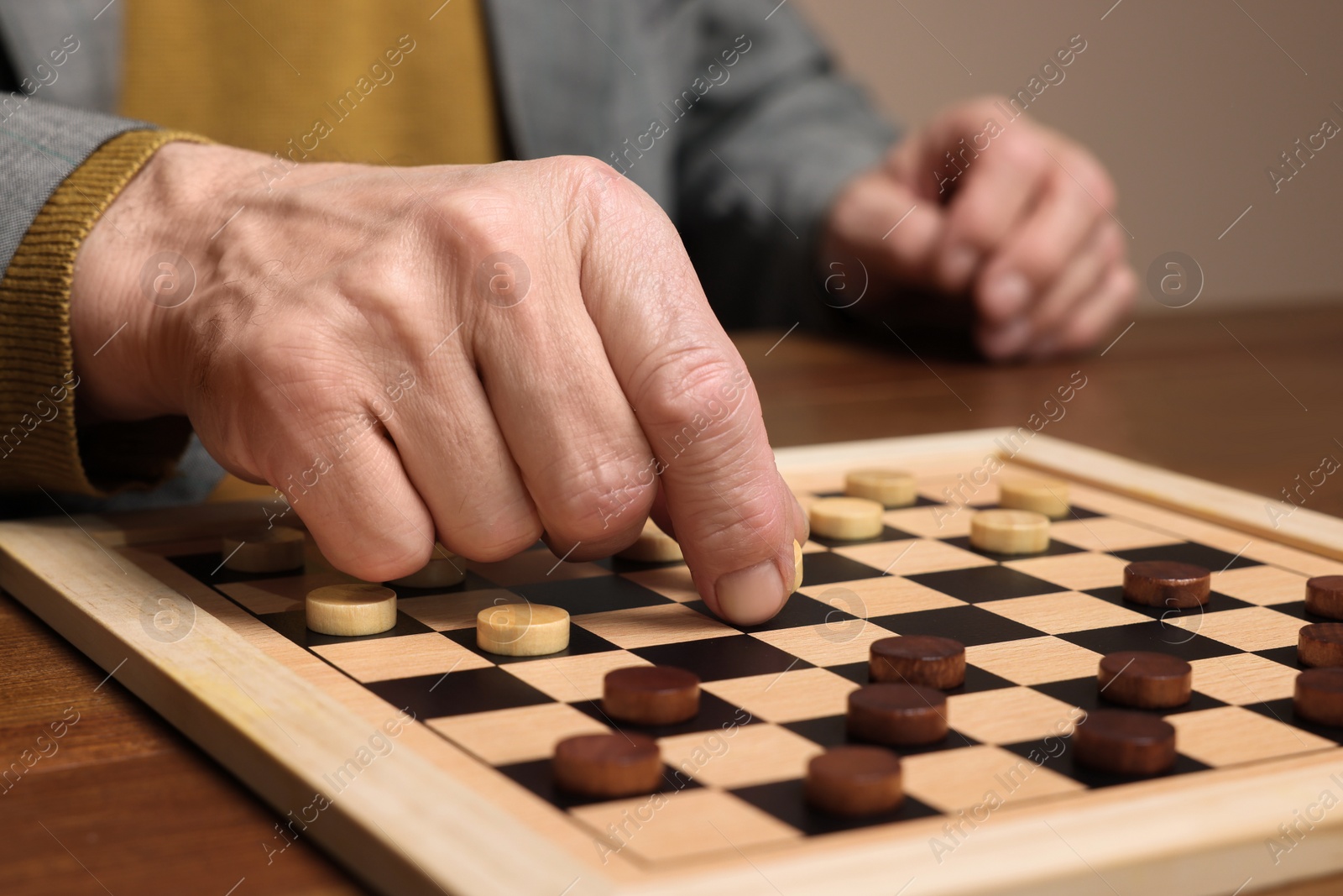 Photo of Playing checkers. Senior man thinking about next move at wooden table, closeup