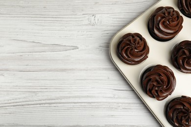 Photo of Delicious chocolate cupcakes with cream in baking tray on white wooden table, top view. Space for text