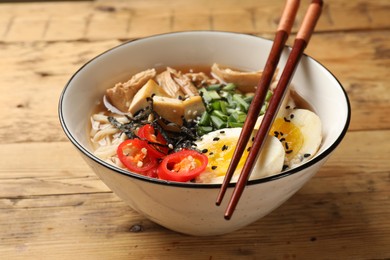 Noodle soup. Bowl of delicious ramen and chopsticks on wooden table, closeup