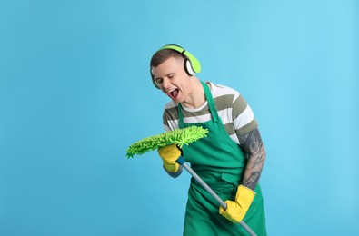 Photo of Handsome young man with headphones and mop singing on light blue background. Space for text