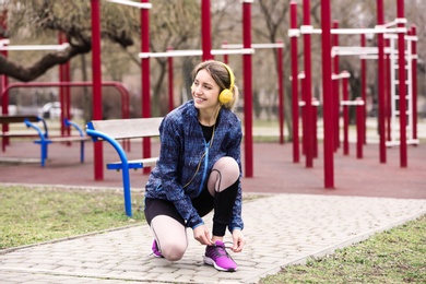 Young woman with headphones tying shoelaces on sports ground