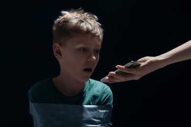 Photo of Kidnapper with phone near little boy taken hostage on dark background
