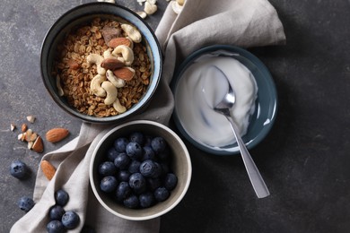 Photo of Tasty granola in bowl, blueberries, yogurt and spoon on gray textured table, flat lay