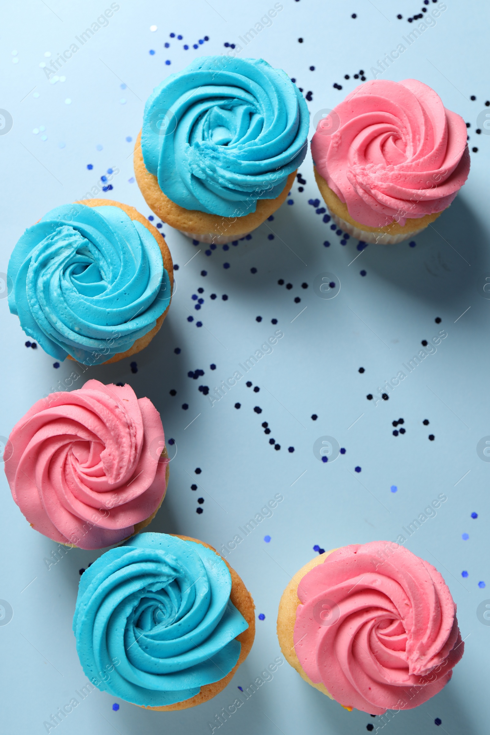 Photo of Delicious cupcakes with bright cream and confetti on light blue background, flat lay. Space for text