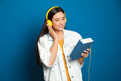 Photo of Young woman listening to audiobook on blue background