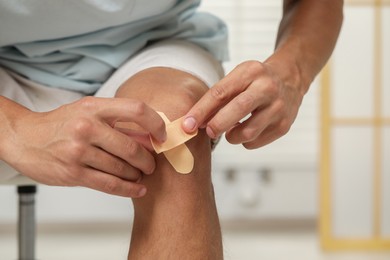 Photo of Man putting sticking plasters onto knee indoors, closeup