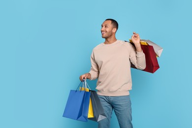 Photo of Happy African American man with shopping bags on light blue background