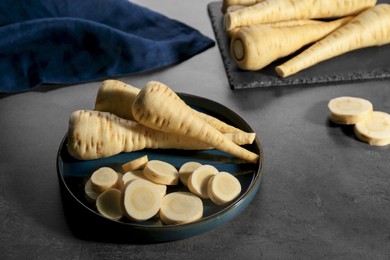 Photo of Whole and cut parsnips on black table