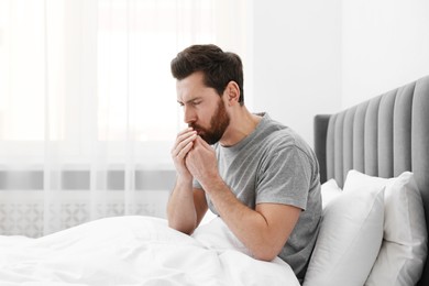 Photo of Sick man coughing on bed at home. Cold symptoms