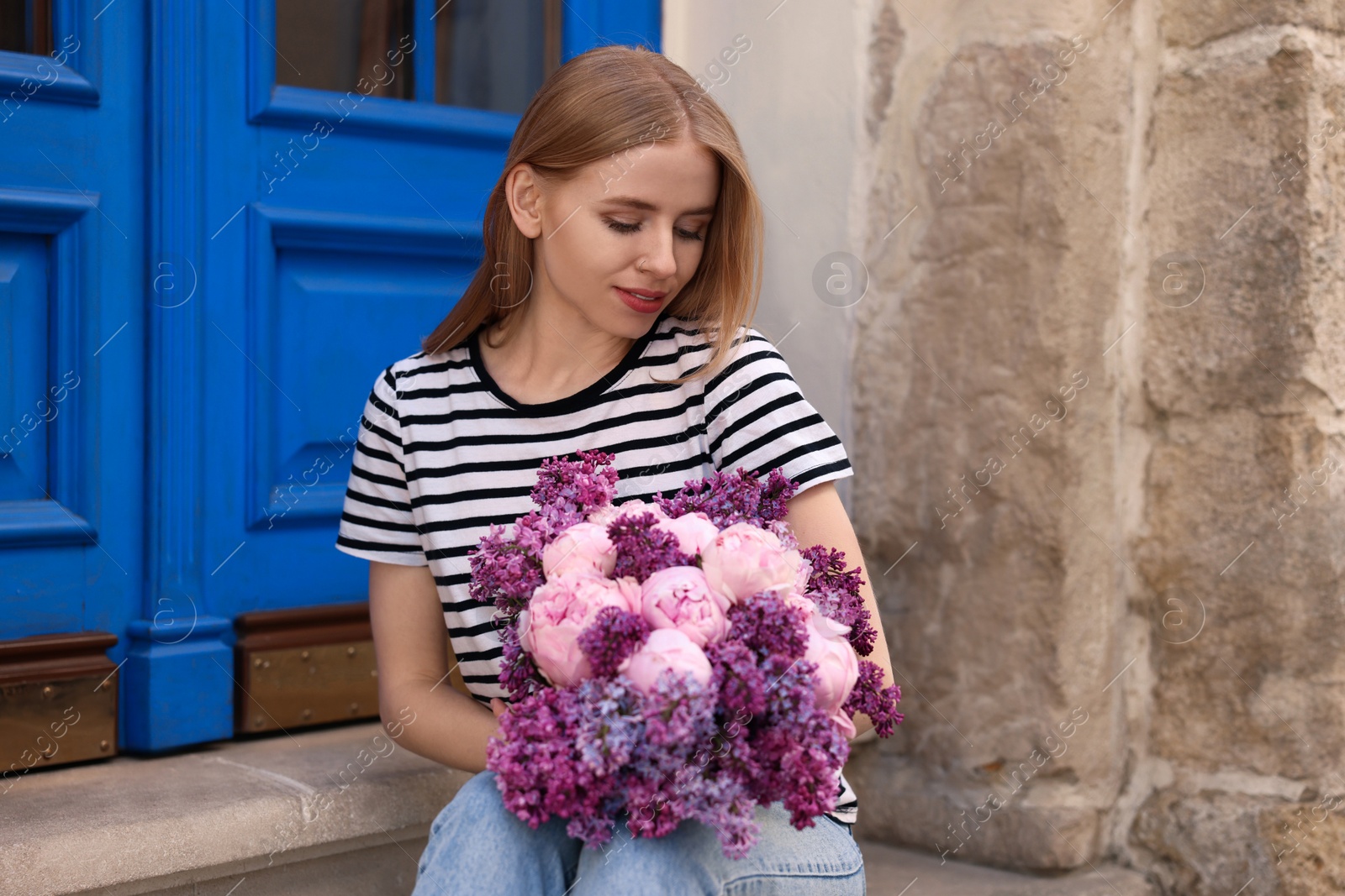 Photo of Beautiful woman with bouquet of spring flowers near building outdoors